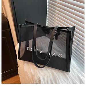 Detalle del bolso tote de malla negra con texto TOTE BAG blanco y cierre magnético