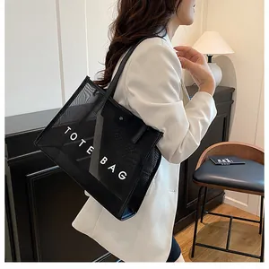 Bolso tote minimalista de malla negra con texto blanco, llevado al hombro con estilo