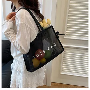 Detalle de bolsa tote de malla negra con texto TOTE BAG blanco llevada por modelo