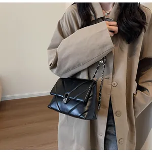 Detail of black V-quilted leather flap bag with silver chain strap on beige trench coat
