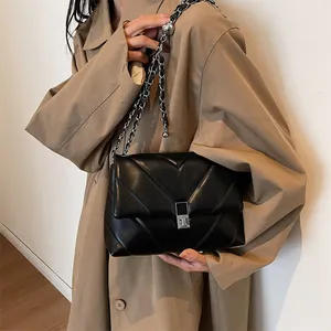 Modern black quilted crossbody bag with silver chain strap shown on a khaki trench coat