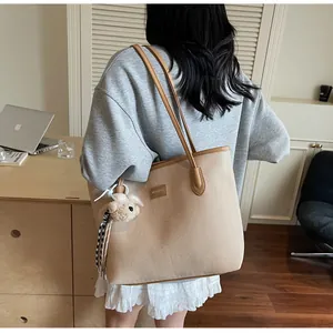 Gros plan sur un cabas beige avec finitions en cuir marron et pendentif ours peluche