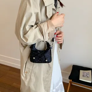 Mini sac seau noir avec nœud et perles porté par un mannequin en trench-coat beige