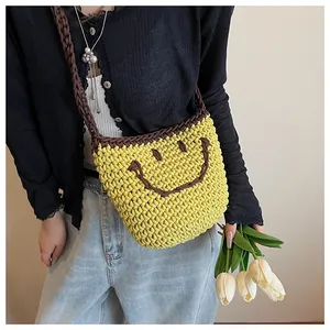 Détail du sac seau jaune tricoté avec motif smiley et bandoulière marron porté