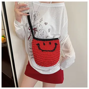 Détail du sac seau rouge tissé main avec un motif smiley noir et une bandoulière tressée