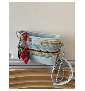 Detail of light blue woven bucket bag with leather base and a cute strawberry charm