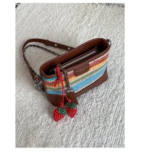 Close-up of rainbow striped woven bag with brown leather trim and red strawberry charms