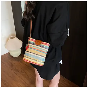 Detail of colorful rainbow striped straw crossbody bag with strawberry pendant and leather flap