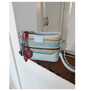 Detail of colorful woven bucket bag featuring a red strawberry pendant and metal chain strap