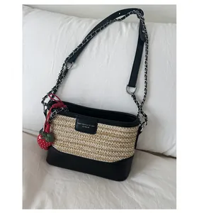 Detailed texture of beige woven straw tote bag with black leather trim and strawberry charm