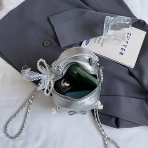 Silver metallic bucket bag with chain strap and pearl bow on gray blazer background