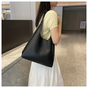 Minimalist black tote bag shown on model with light yellow top and white skirt