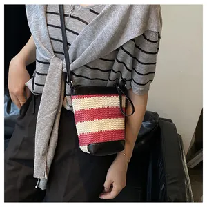 Detailed view of woven bucket bag with red and white stripes and black leather strap
