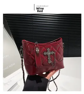 Detail of wine red quilted shoulder bag featuring metal cross and skull zipper charm