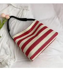 Détail du sac de plage en paille rayé rouge et blanc avec bandoulière noire sur tissu blanc