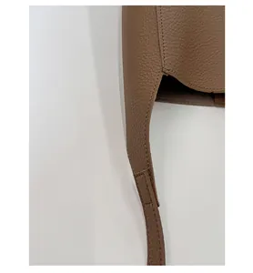Gros plan d'un sac seau en cuir marron grainé montrant les coutures et les détails de bandoulière