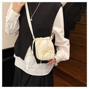 Detail van de crèmekleurige crossbodytas met strik en trekkoord op een model