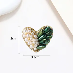 Detail of heart-shaped brooch with white pearls, green crystal, and 3x3.3cm dimensions