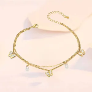 Detail of double-layer gold anklet featuring butterfly charms and pearl accents with lobster clasp