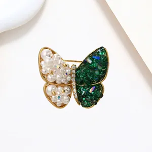 Close-up of golden butterfly brooch with white pearls and emerald green crystals