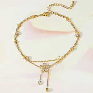 Detail of gold layered anklet with zircon flower pendant and elegant tassel fringe