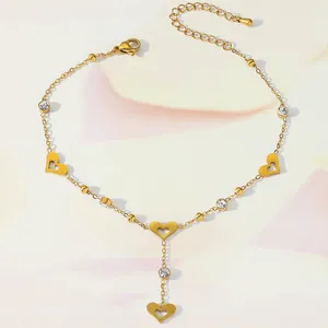 Detail of gold ankle chain featuring hollow heart charms and round zircon crystals
