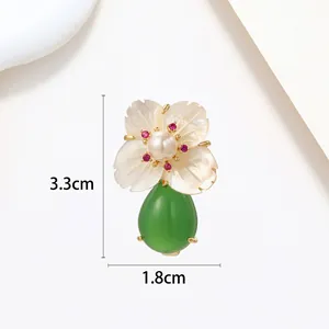 Macro view of flower brooch with pearl petal, red crystal accents and green drop pendant