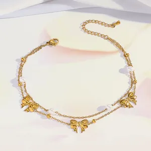 Detail of double-layer gold anklet featuring bow charms, pearls and adjustable chain extender