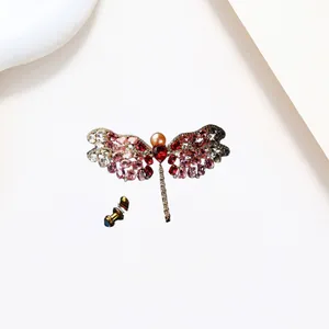 Macro detail of dragonfly pearl brooch with red and pink gemstones on white background