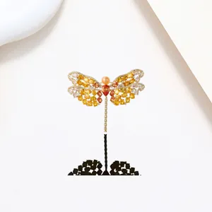 Macro shot of dragonfly brooch with yellow pavé crystals and pearl on white background