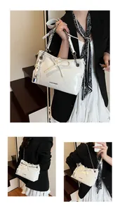 Detail of white glossy shoulder bag featuring silver chain, lock charm and bow accent