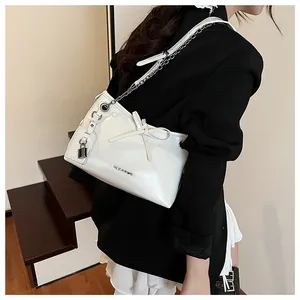 Detail of white glossy leather handbag with bow, metal padlock charm and chain strap