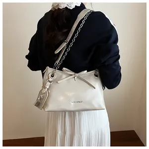 Detail of a creamy white leather tote bag with a bow and silver chain strap on a model