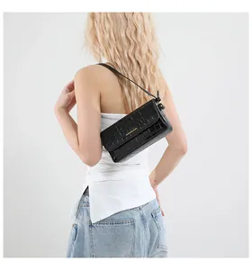 Model trägt eine schwarze Tasche mit Krokostruktur, Goldaufdruck und Lederriemen