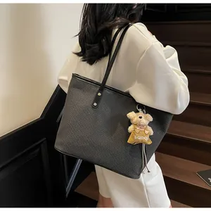 Detailed texture of black leather tote bag featuring a cute plush bear charm accessory