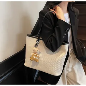 Side view of woven tote bag with leather straps and a cute plush bear charm