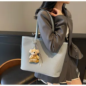 Detail of light blue woven tote bag with a soft plush bear charm and high-capacity design
