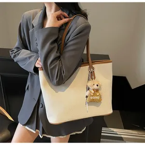 Detail of woven beige tote bag with brown leather trim and cute bear charm pendant