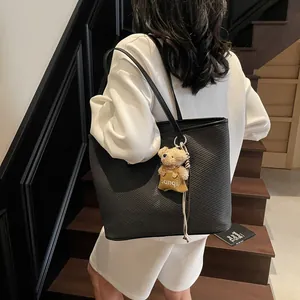 Minimalist black tote bag with textured faux leather and a plush bear charm on a model