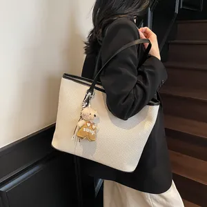 Minimalist beige woven tote bag with black trim and plush bear charm for daily commuting