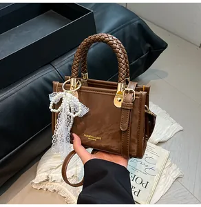 Detailed close-up of brown glossy leather handbag with woven handle and pearl bow charm