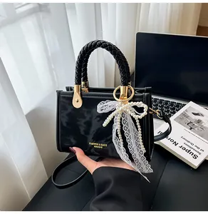 Detail of a black glossy handbag with a pearl lace bow and stylish woven handle