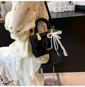 Detail of black glossy handbag with woven handle and elegant white lace bow pendant