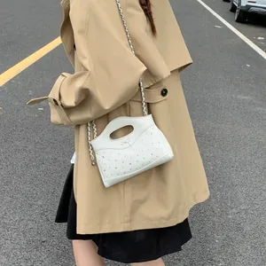 Quilted white chain bag with crystal studs and bow detail worn with a trench coat