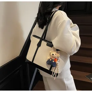 Detail of cream woven tote bag with black leather trim and cute plush bear charm decoration