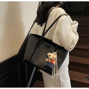 Detail of black woven tote bag featuring a cute bear charm and premium leather strap