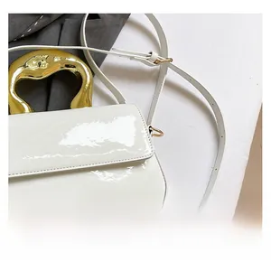 Detailed view of white patent leather handbag with artistic irregular gold metal handle