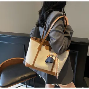 Detail of a large beige woven tote bag with brown leather handles and a bear charm accessory