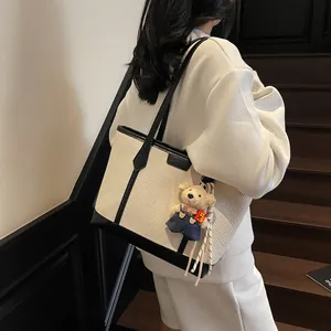 Minimalist beige woven tote bag with black leather trim and cute bear charm pendant