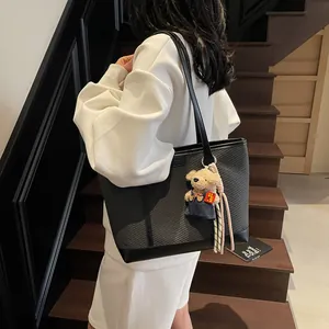 Large black minimalist tote bag with texture and teddy bear charm on model shoulder